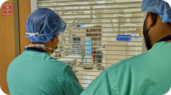 Two EVS team members peering through the window of an operating room while the ADIBOT A1 fully autonomous UV-C disinfection robot is disinfecting the room.