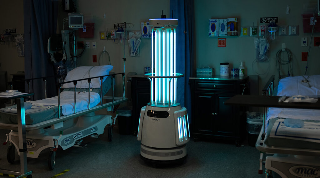 The ADIBOT A1 fully autonomous UV-C disinfection robot situated between two patient beds in a hospital with UV-C lamps turned on.