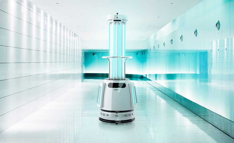 The ADIBOT A1 fully autonomous UV-C disinfection robot with UV-C lamps turned on in the middle of a bright and reflective hallway corridor.
